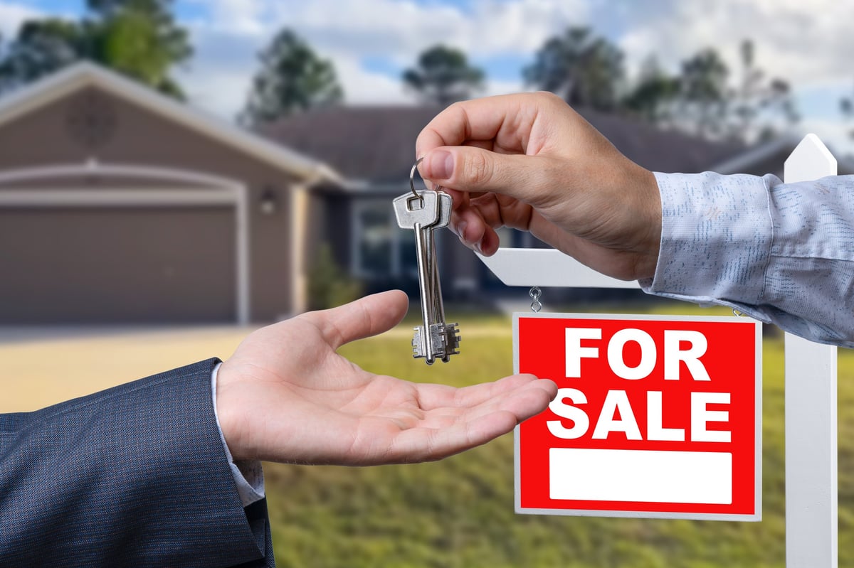 Real Estate Agent Handing Over the House Keys in Front of a Beautiful New Home and For Sale Real Estate Sign